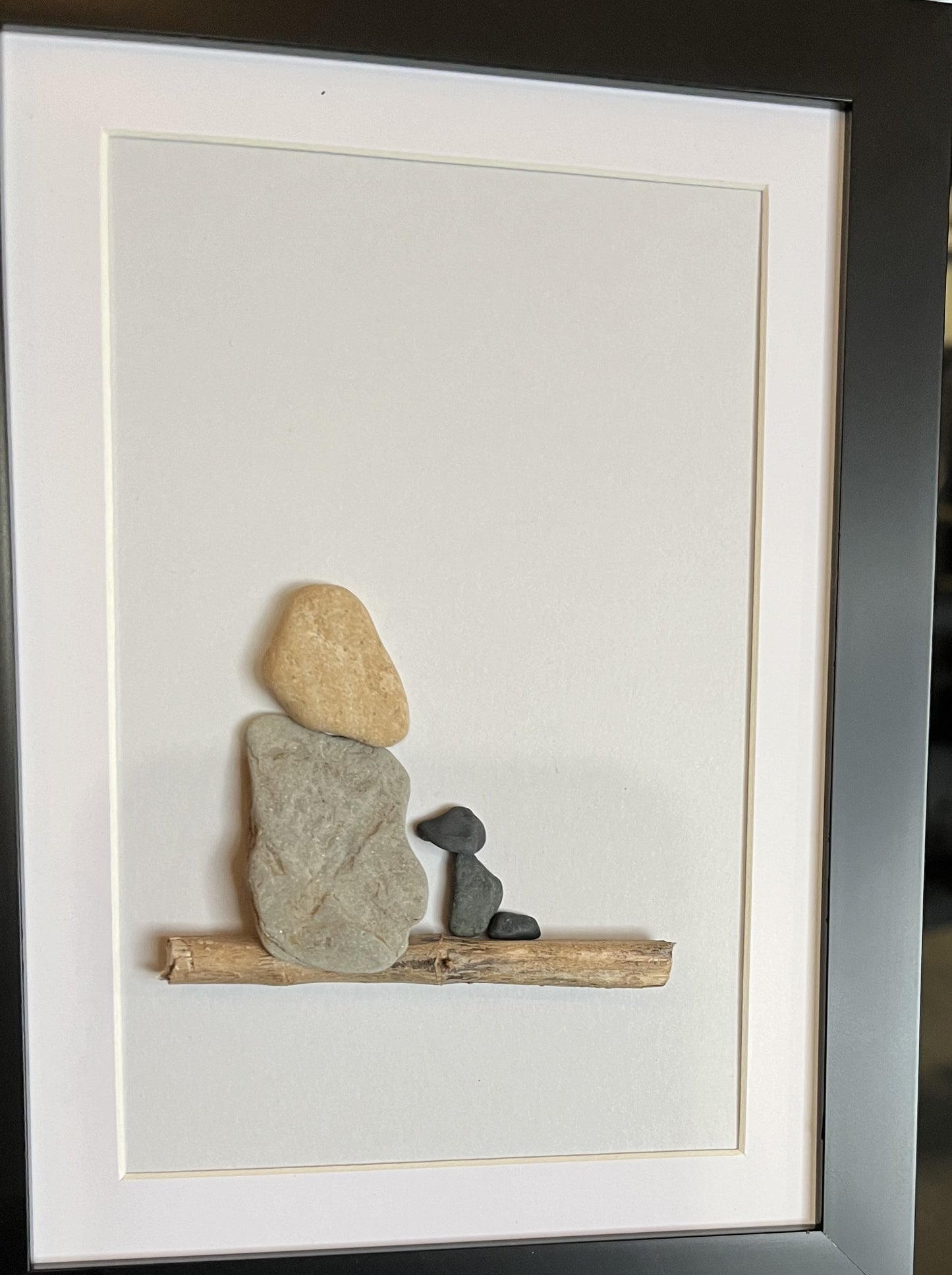 lady with blonde hair sitting on a log with black dog pebble art