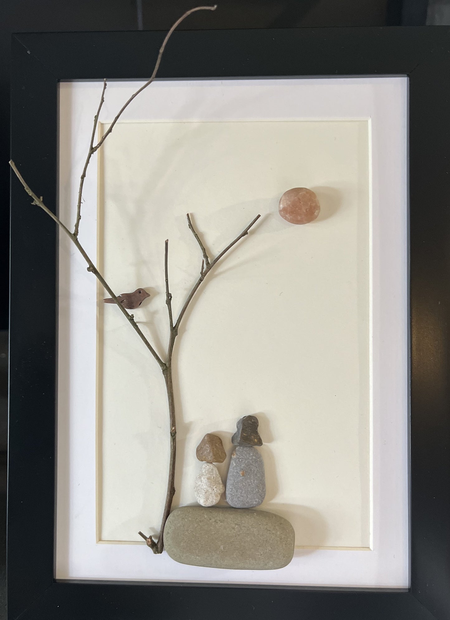 family pebble art with mother with dark hair and child with brown hair under a tree branch with a bird looking at the sun